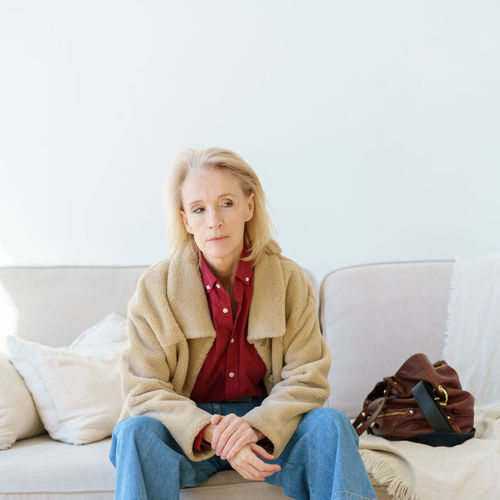 Tired senior woman looking aside while resting on sofa at home after hard working day
