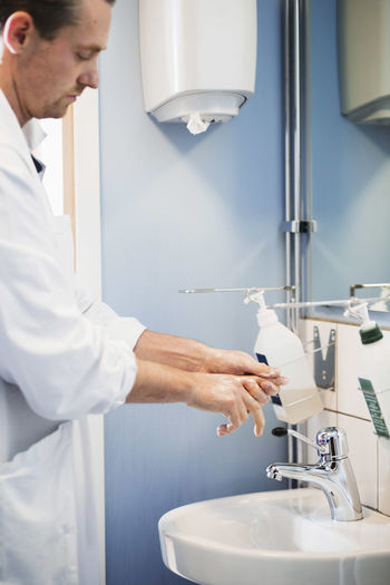 Side view of male doctor washing hands in hospital bathroom