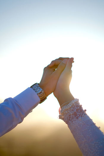 Close-up of hand holding hands against sky