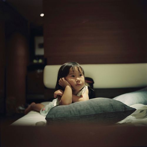 Cute girl looking away while lying on bed at home