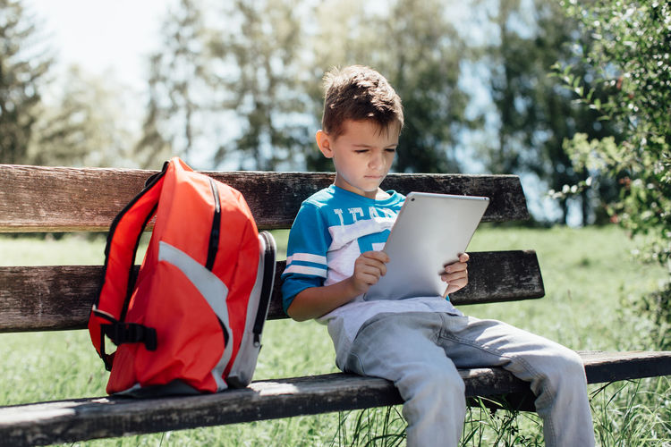 Boy sitting with digital tablet on bench