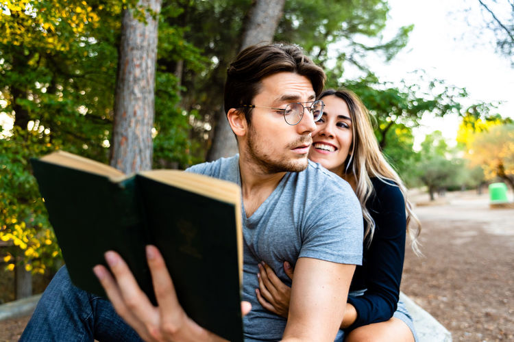 Woman embracing boyfriend reading book at park