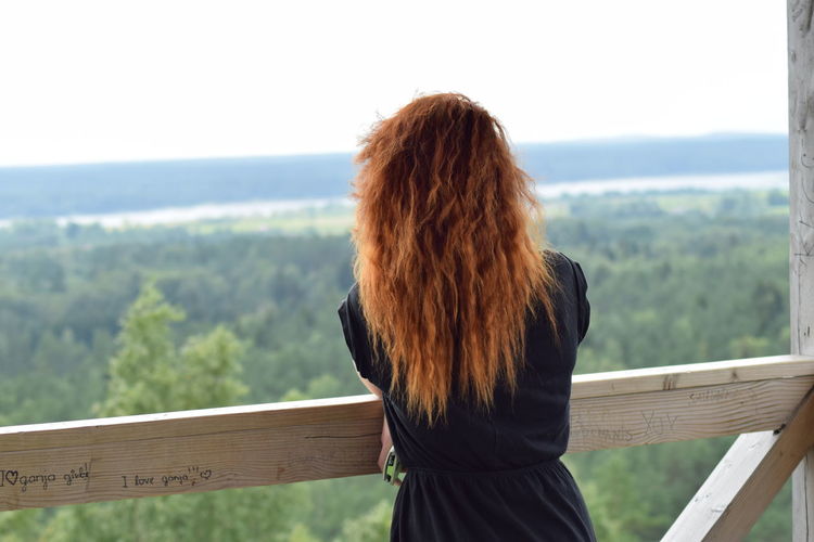 Rear view of woman leaning on railing against green landscape
