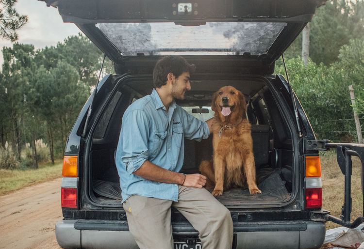 Young man with dog in car trunk