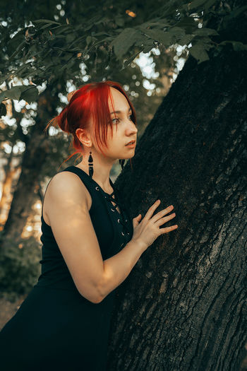 Portrait of young woman standing against tree trunk