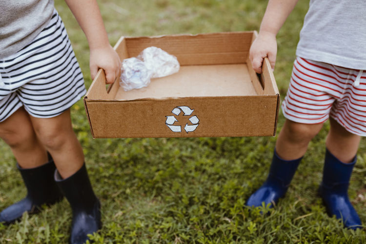 Boys collecting plastic in cardboard box with recycling symbol