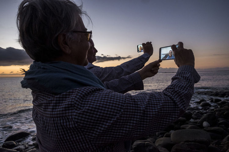 Couple taking selfie from mobile phones at beach during sunset