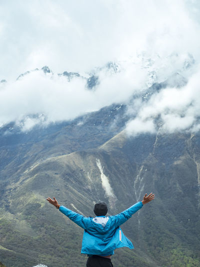 Rear view of man with arms outstretched standing on mountain against cloudy sky