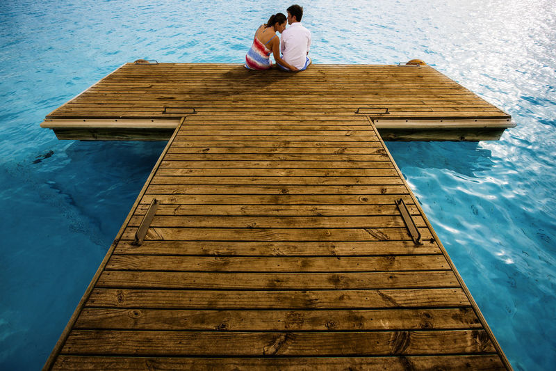 Rear view of man and woman sitting on pier over sea at beach