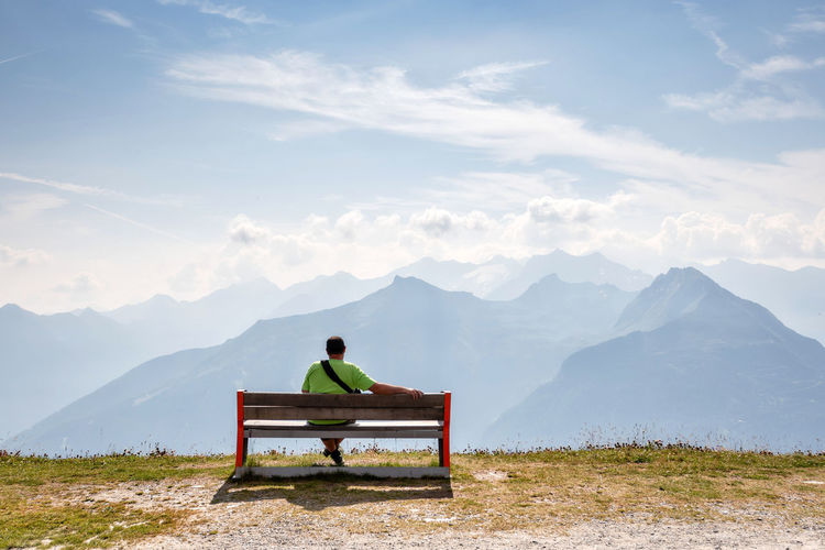 Rear view of man sitting on bench against mountains