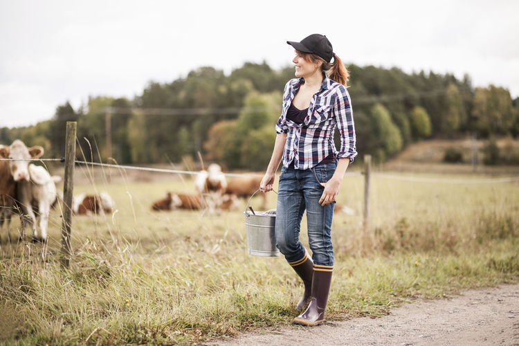 Female farmer with bucket walking while animals grazing in field
