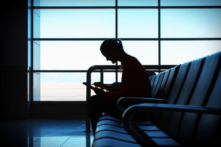 Woman using digital tablet while sitting on chair in airport lobby