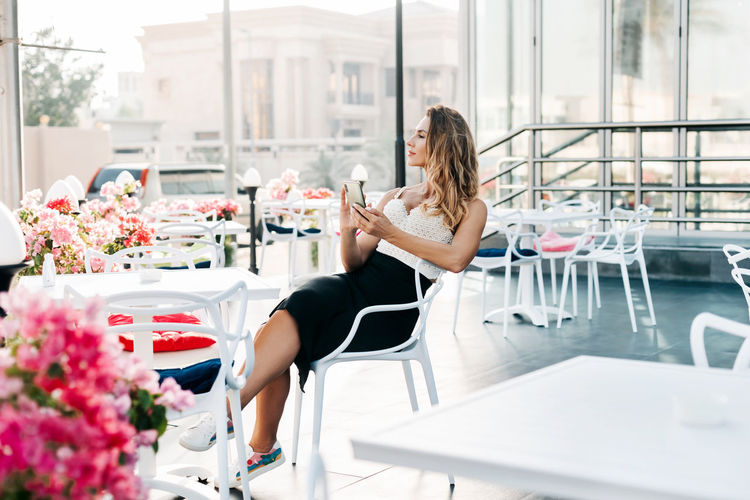 An attractive woman sits in a street cafe and uses her phone to exchange messages