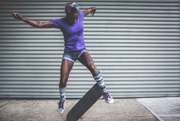Full length of woman skateboarding against shutter