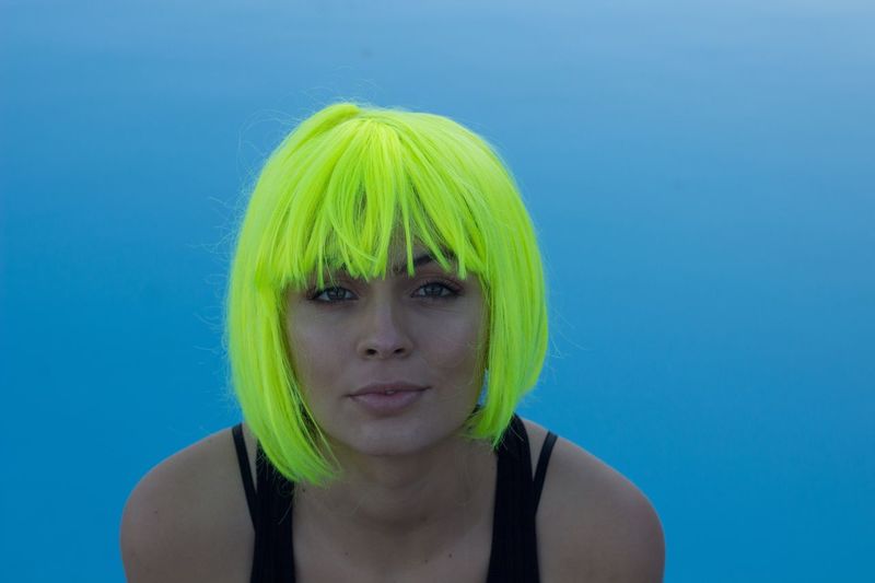 Low angle portrait of beautiful woman with green hair against clear blue sky