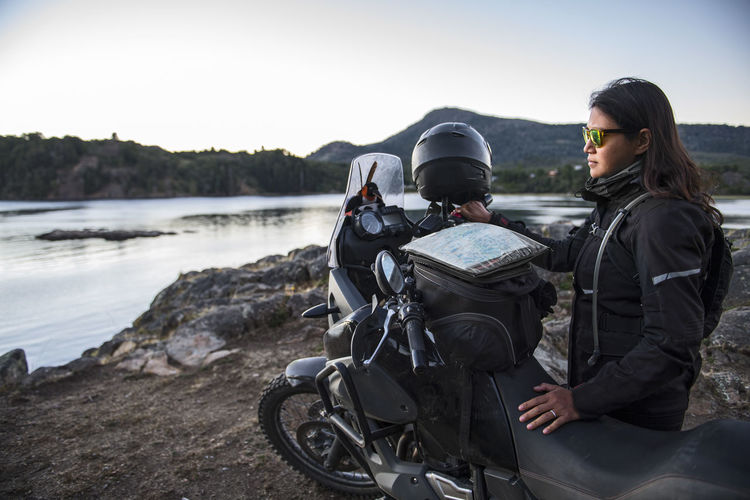 Woman standing next to touring motorbike at lago alumine in argentina