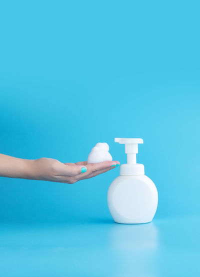 Close-up of hand holding bottle against blue background