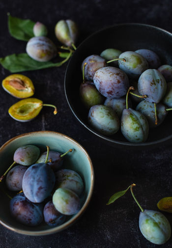 Close up of bowls of fresh plums against a black background.