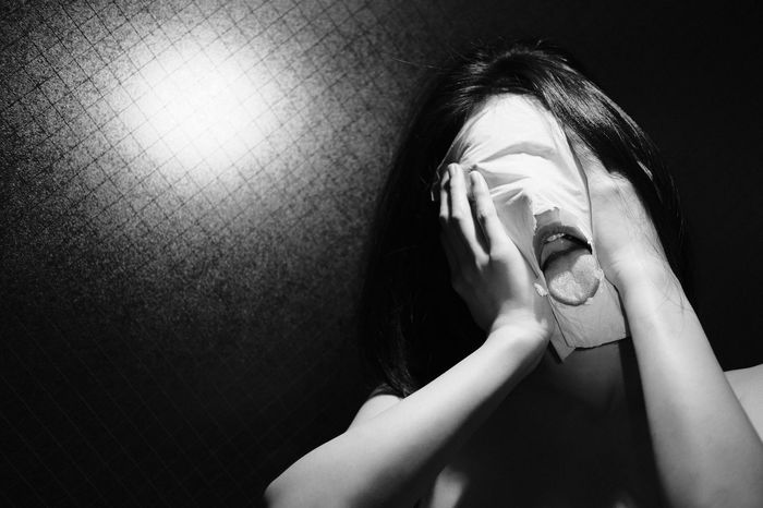 Close-up of woman sticking out tongue while covering face with tissue paper in darkroom