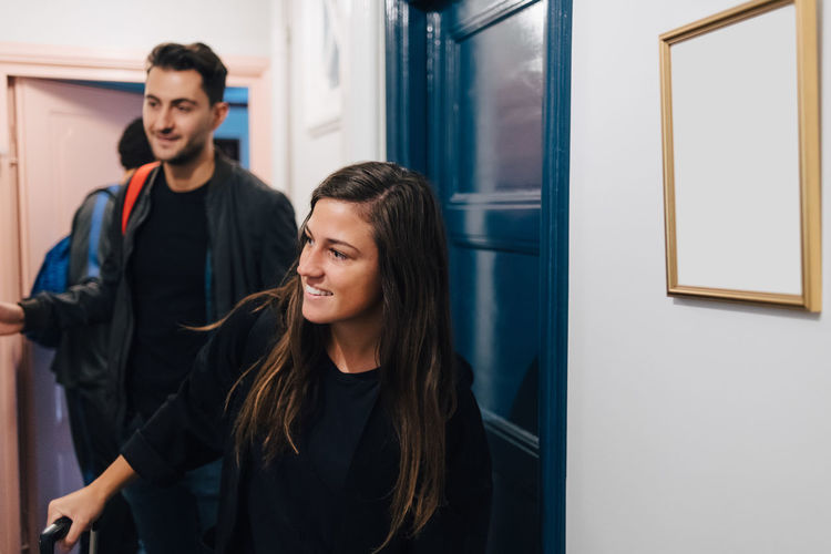 Smiling young woman with male friends arriving at rental apartment