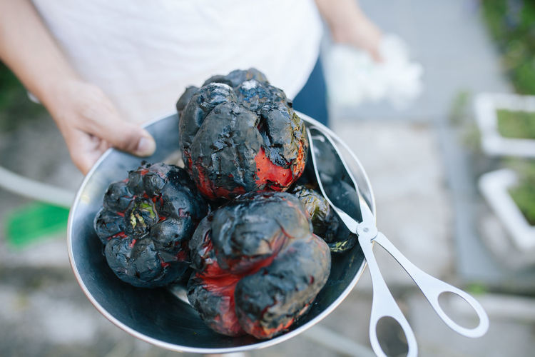 Midsection of person holding grilled bell peppers in bowl while standing outdoors