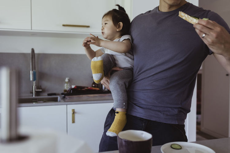 Midsection of father eating food while carrying son in kitchen