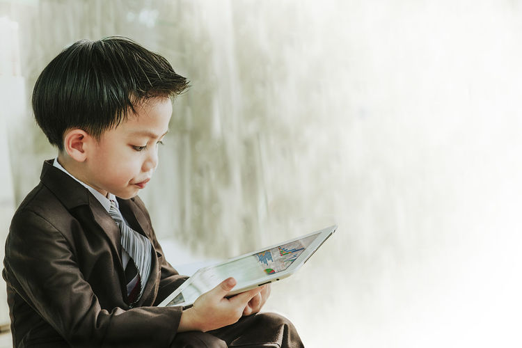 Boy holding digital tablet while sitting on floor