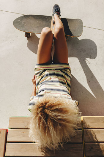 Blond afro woman reclining with skateboard on sunny day