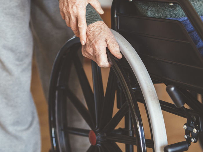Midsection of woman assisting senior man sitting on wheelchair
