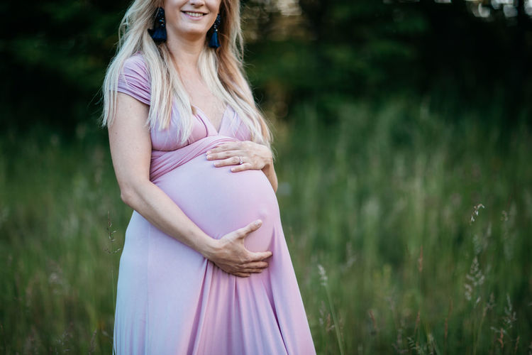 Happy pregnant woman standing on field