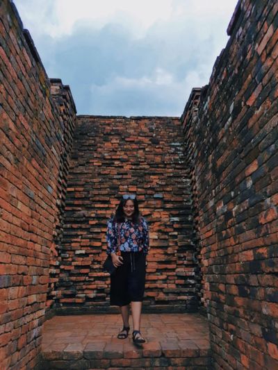 Full length portrait of young woman standing against brick wall