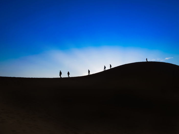 Silhouette people on desert against blue sky