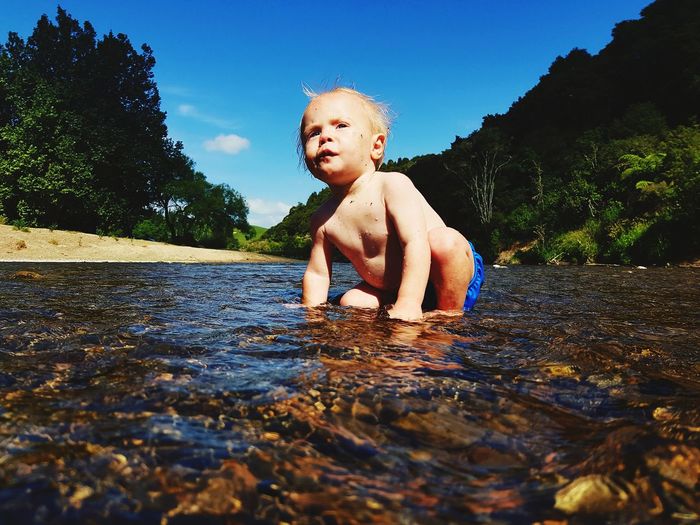 Full length of shirtless boy in lake against sky