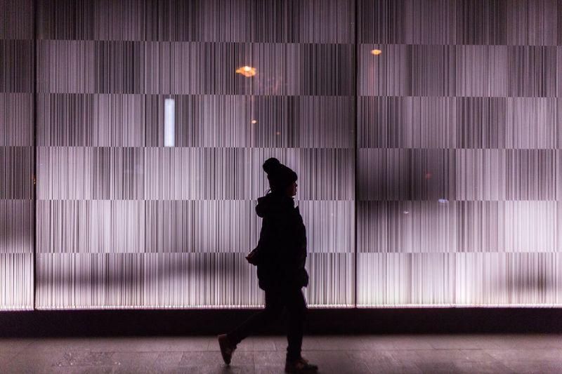 Side view of silhouette woman walking on footpath by patterned glass
