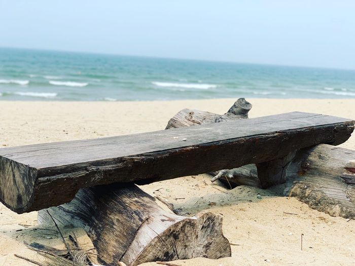 Driftwood on beach by sea against sky