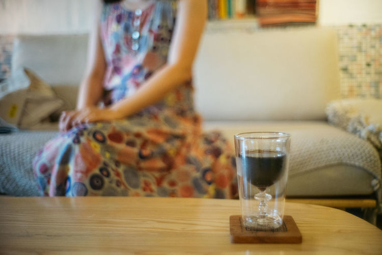 Midsection of woman drinking glass on table at home