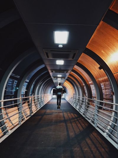 Rear view of man walking on illuminated underground walkway