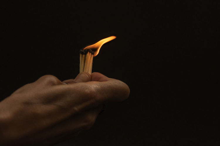 Close-up of hand holding candle against black background