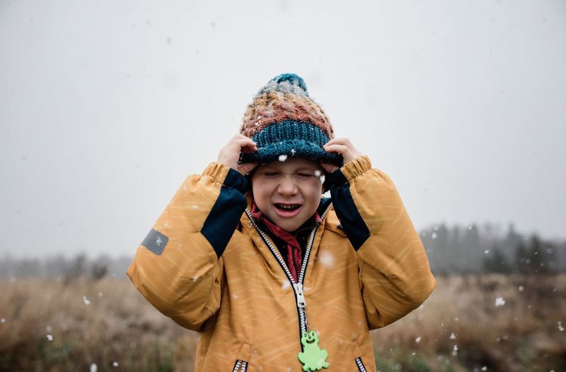 Boy pulling his hat over his face laughing playing in the snow
