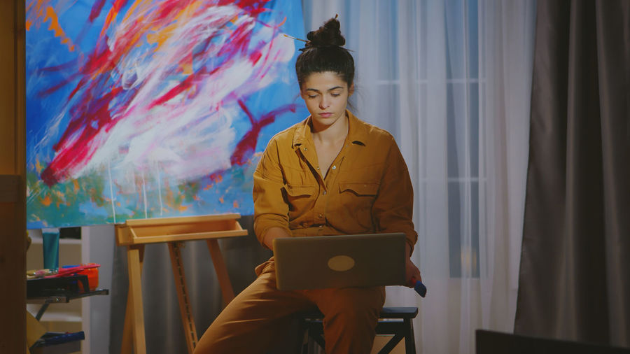 Woman using laptop against painting