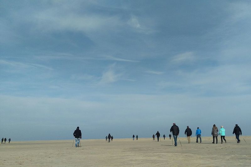 Rear view of people walking on sand against blue sky at beach