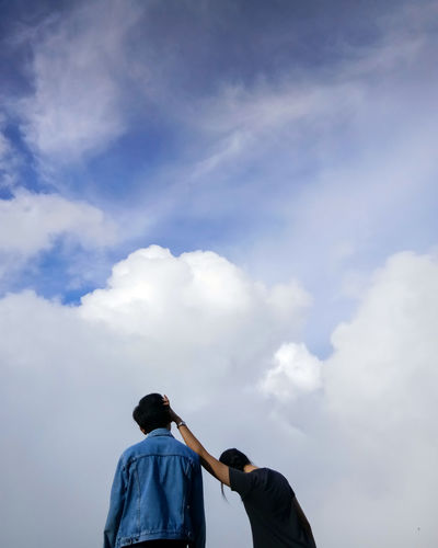 Low angle view of friends standing against cloudy sky