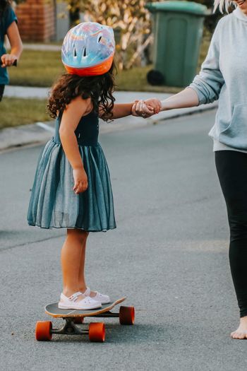 Little girl getting help from her mum while learning to ride a skateboard