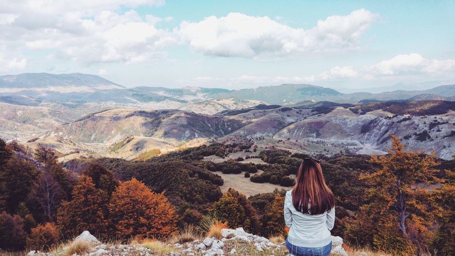 Rear view of woman sitting on mountain against cloud sky