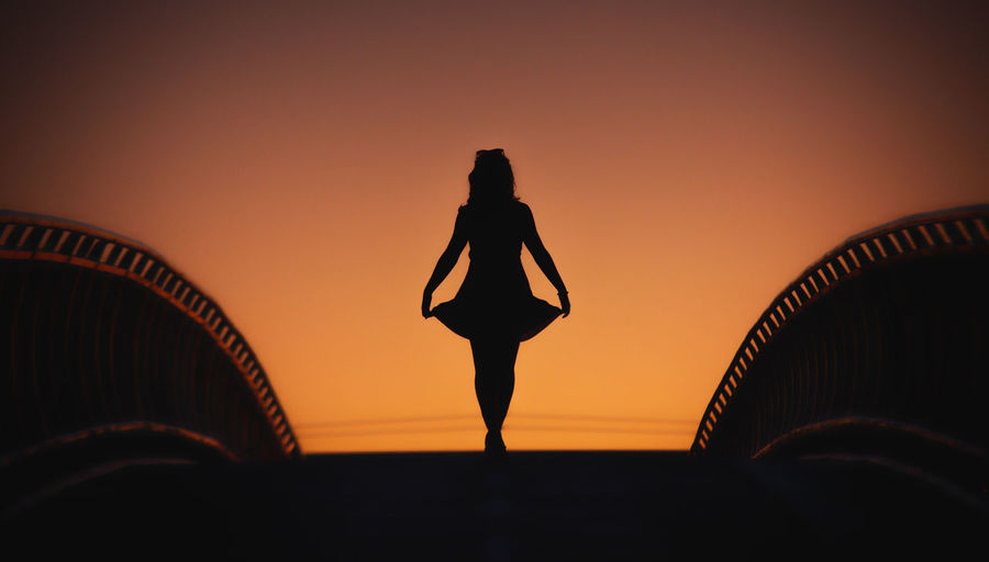Silhouette woman standing on footbridge against sky during sunset