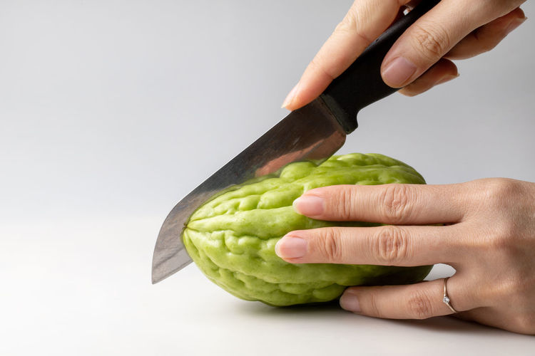 Cropped image of hand holding green pepper against white background