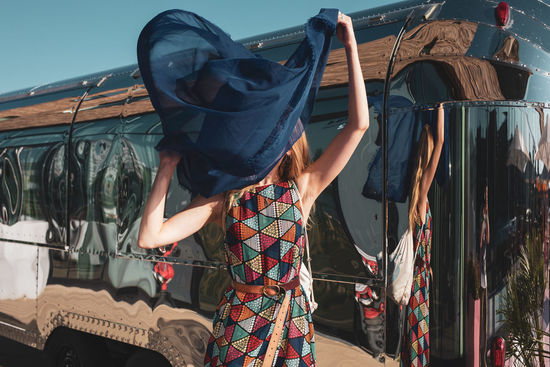 Woman holding blue scarf standing against bus