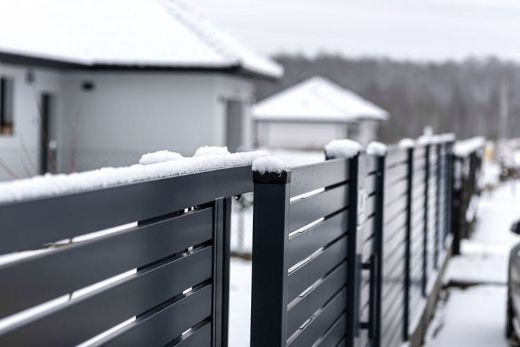 Modern anthracite panel fence with falling snow, visible sliding gate.