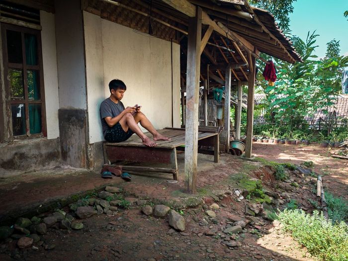 Side view of young man sitting on abandoned house