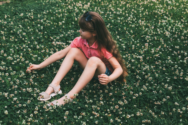 A cute adorable girl sits on a clover meadow and collects a bouquet. rest and relaxation in nature. 